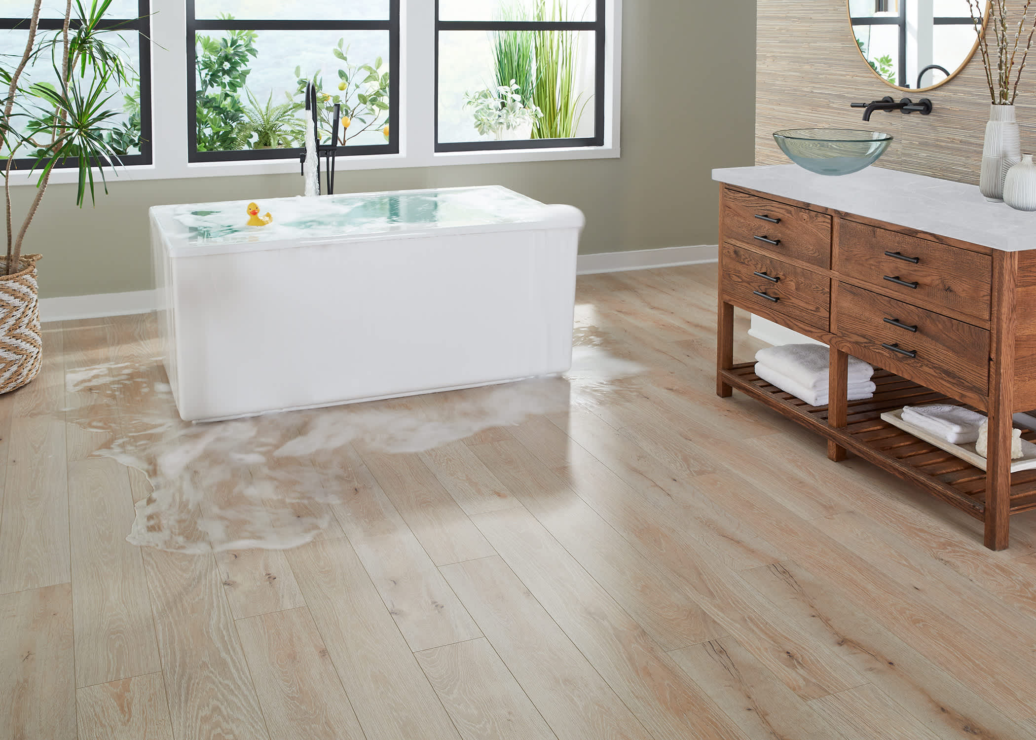 Blonde waterproof rigid vinyl plank floor in bathroom with water overflowing from freestanding tub and vessel sink
