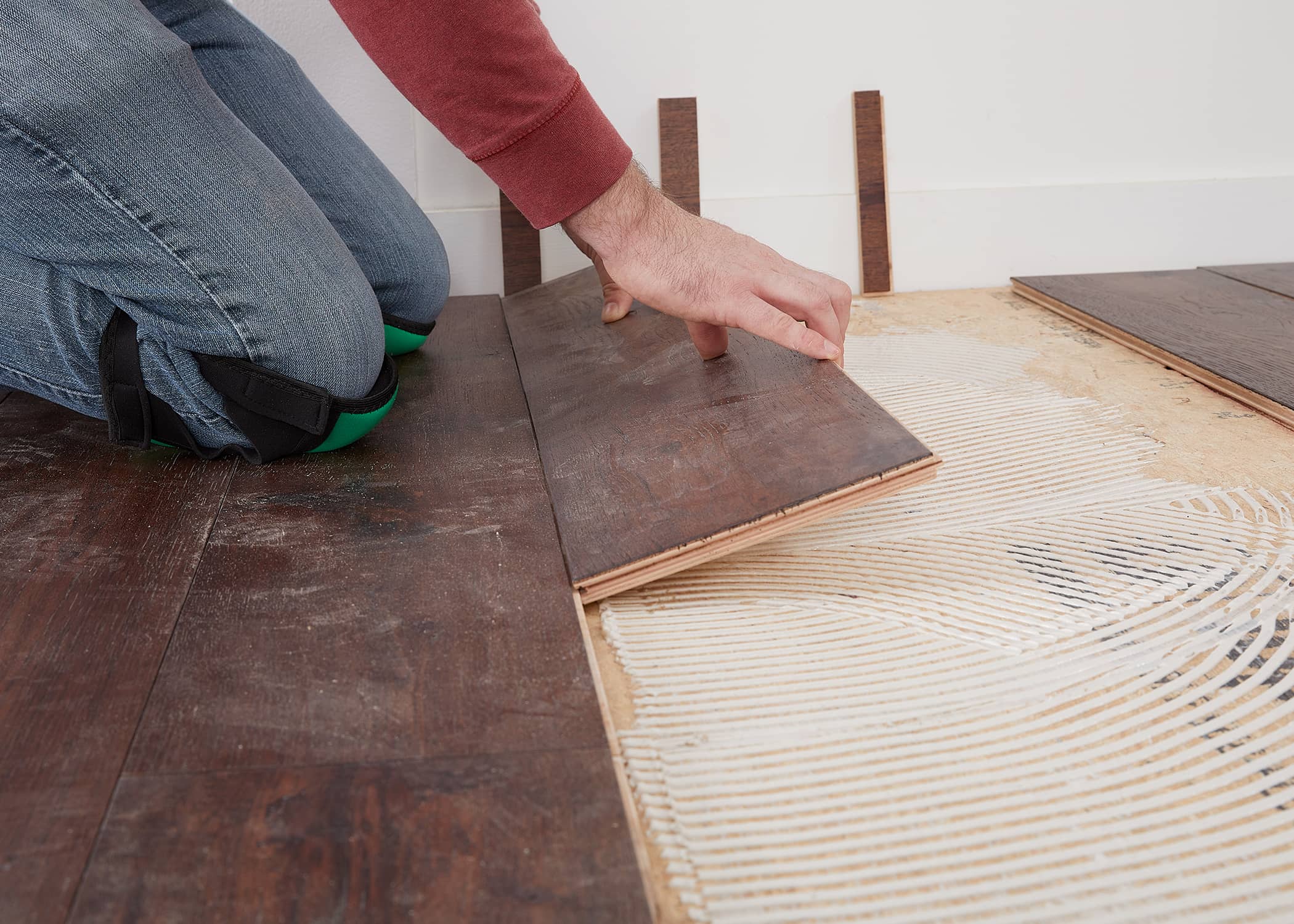 person installing dark brown hard surface floor over glue