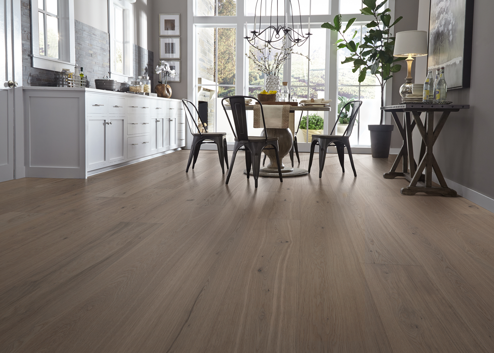 brown water resistant engineered hardwood floor in kitchen with round dining table and gray metal chairs plus white lower cabinets and brick backsplash plus dark gray walls