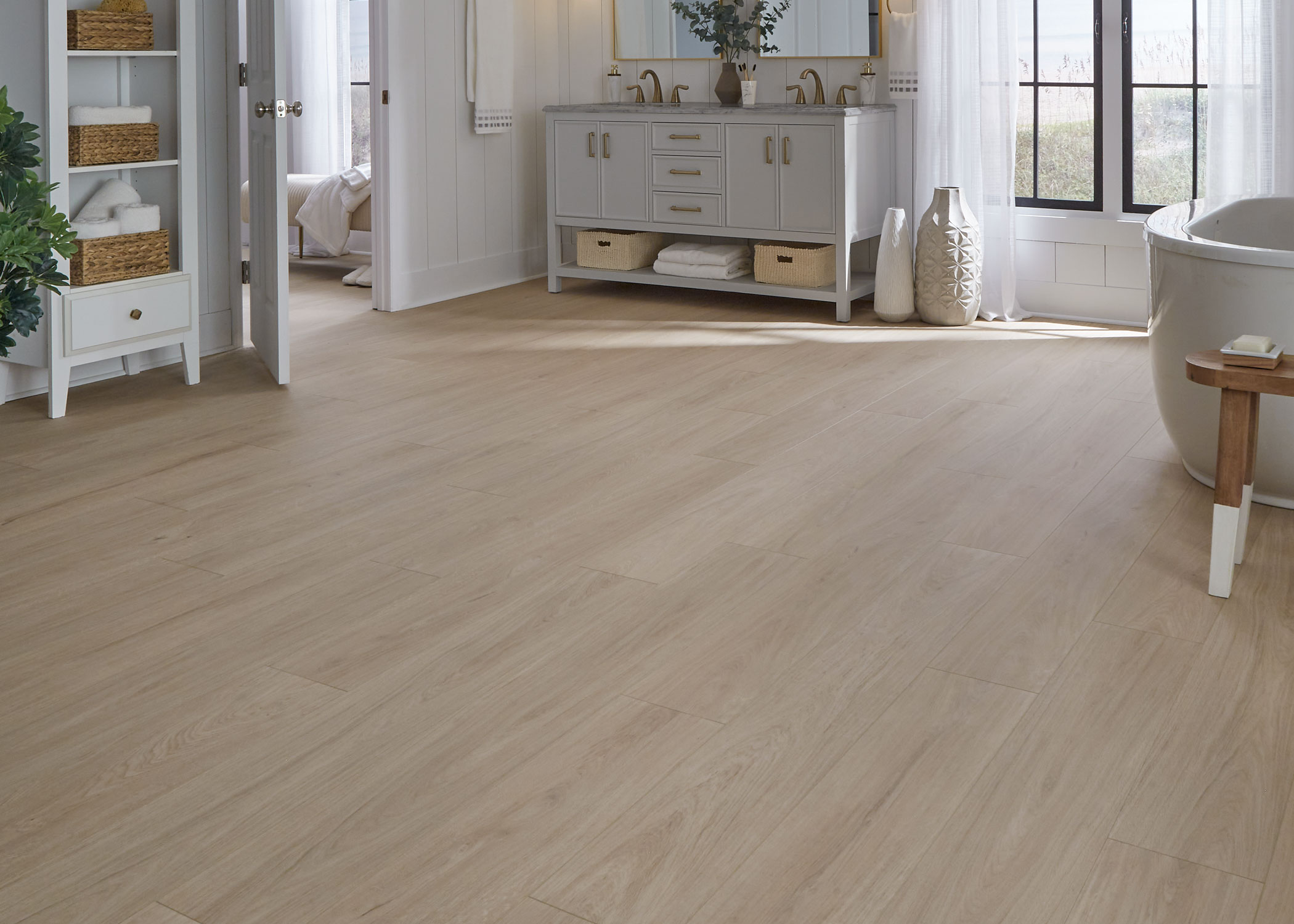 blonde waterproof rigid vinyl plank floor in bathroom with light gray dual vanity plus oval freestanding tub and small light wood stool and shiplap walls