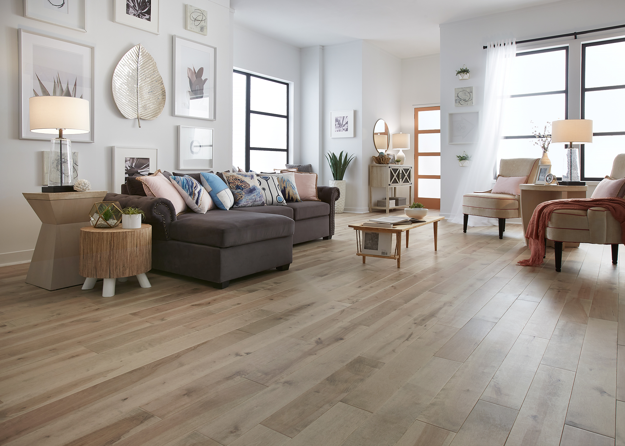 blonde solid hardwood floor in living room with dark gray sectional with pink and blue accent pillows plus beige accent chairs and art gallery wall