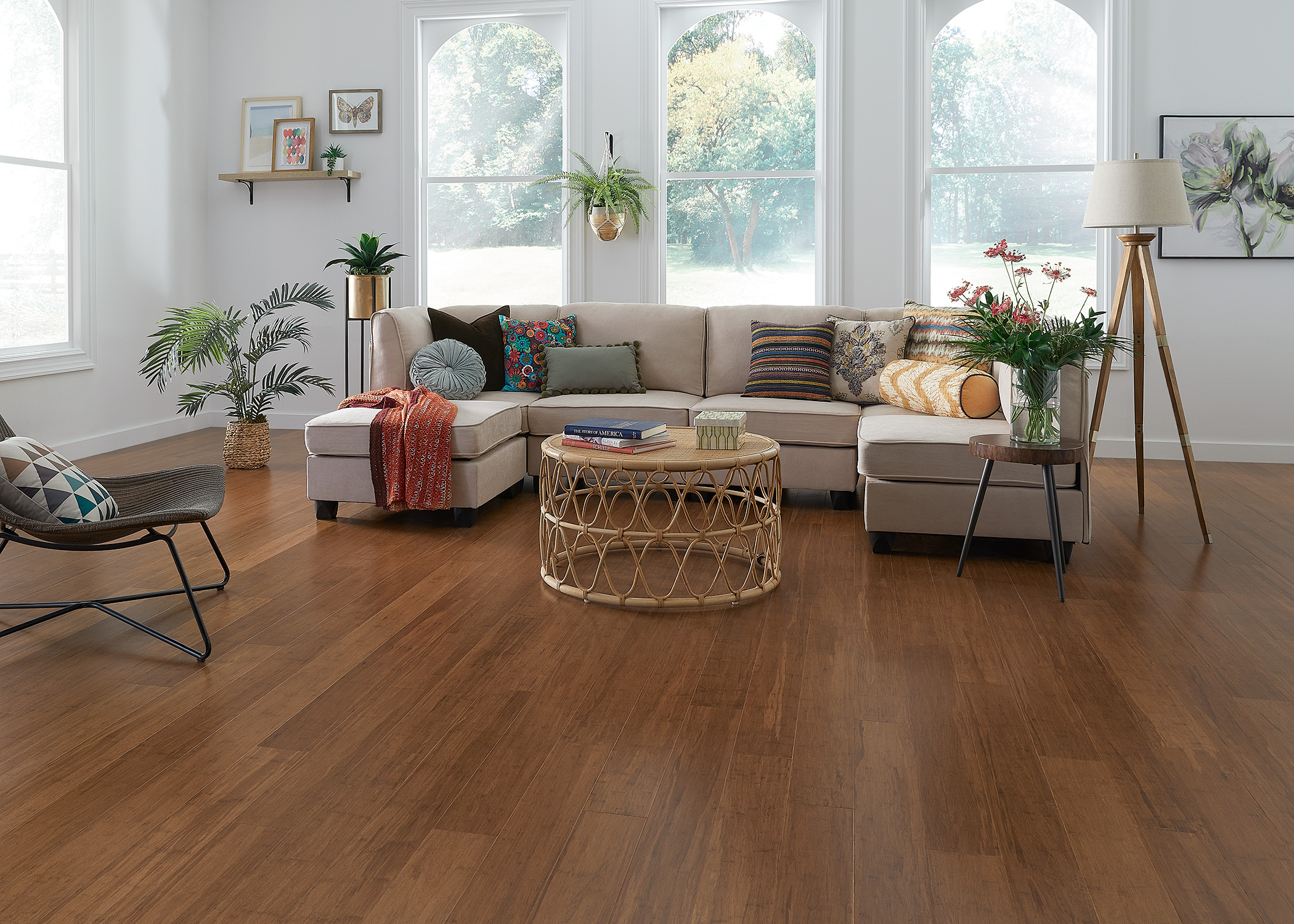 reddish brown bamboo flooring in living room with taupe sectional with colorful accent pillows and rattan coffee table and tripod wood floor lamp