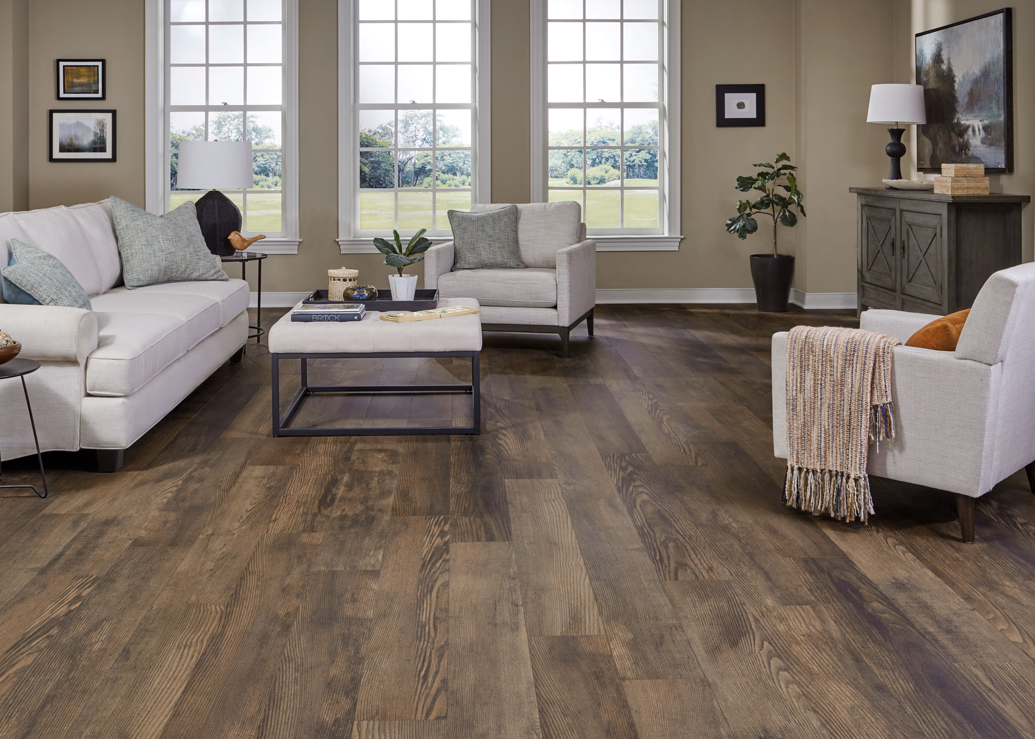 medium brown waterproof hybrid resilient flooring in living rom with beige furnishings with upholstered cocktail table plus dark brown cabinet and potted plant