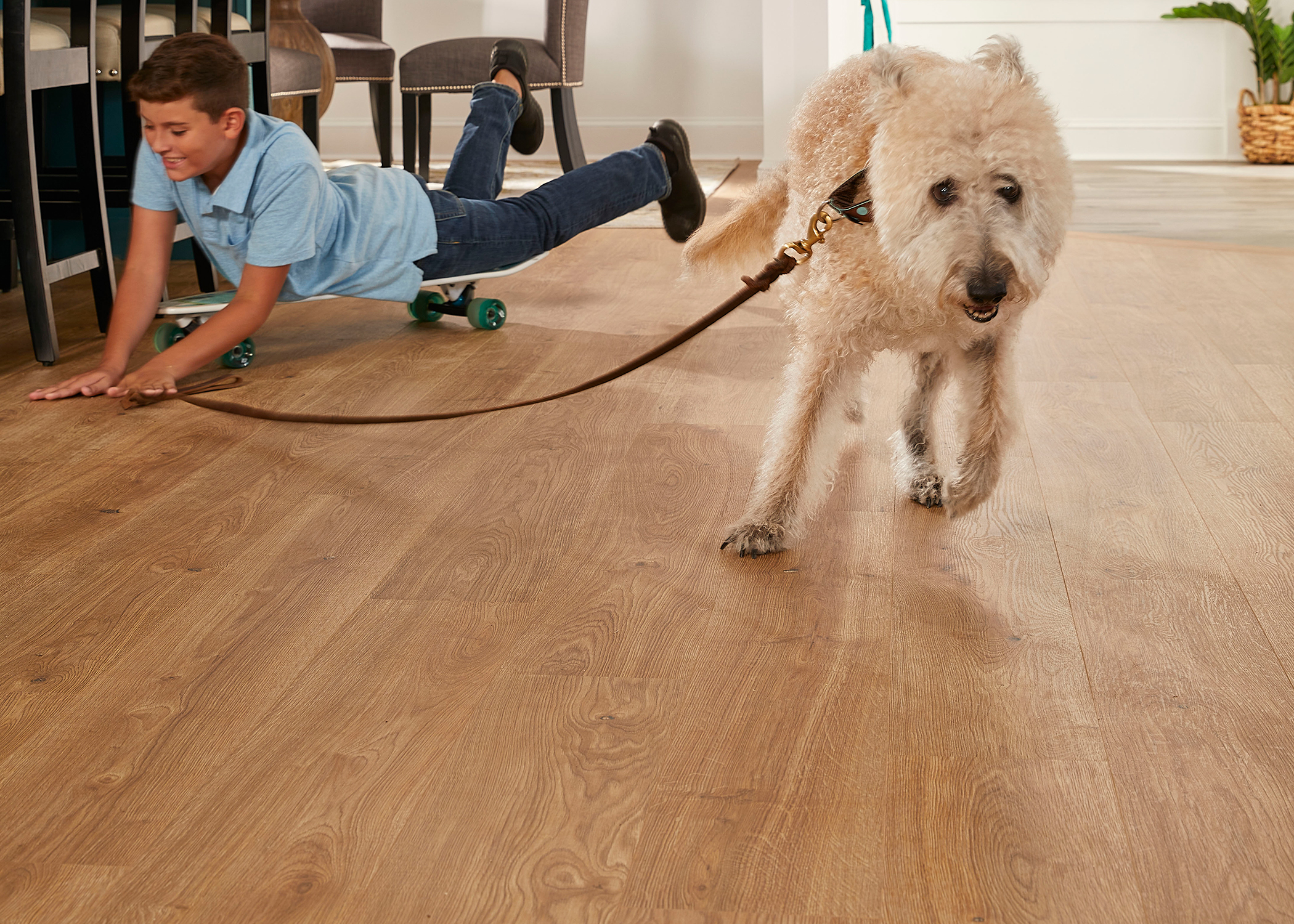 light brown waterproof hybrid resilient flooring in living area with boy on skateboard being pulled by blonde dog 