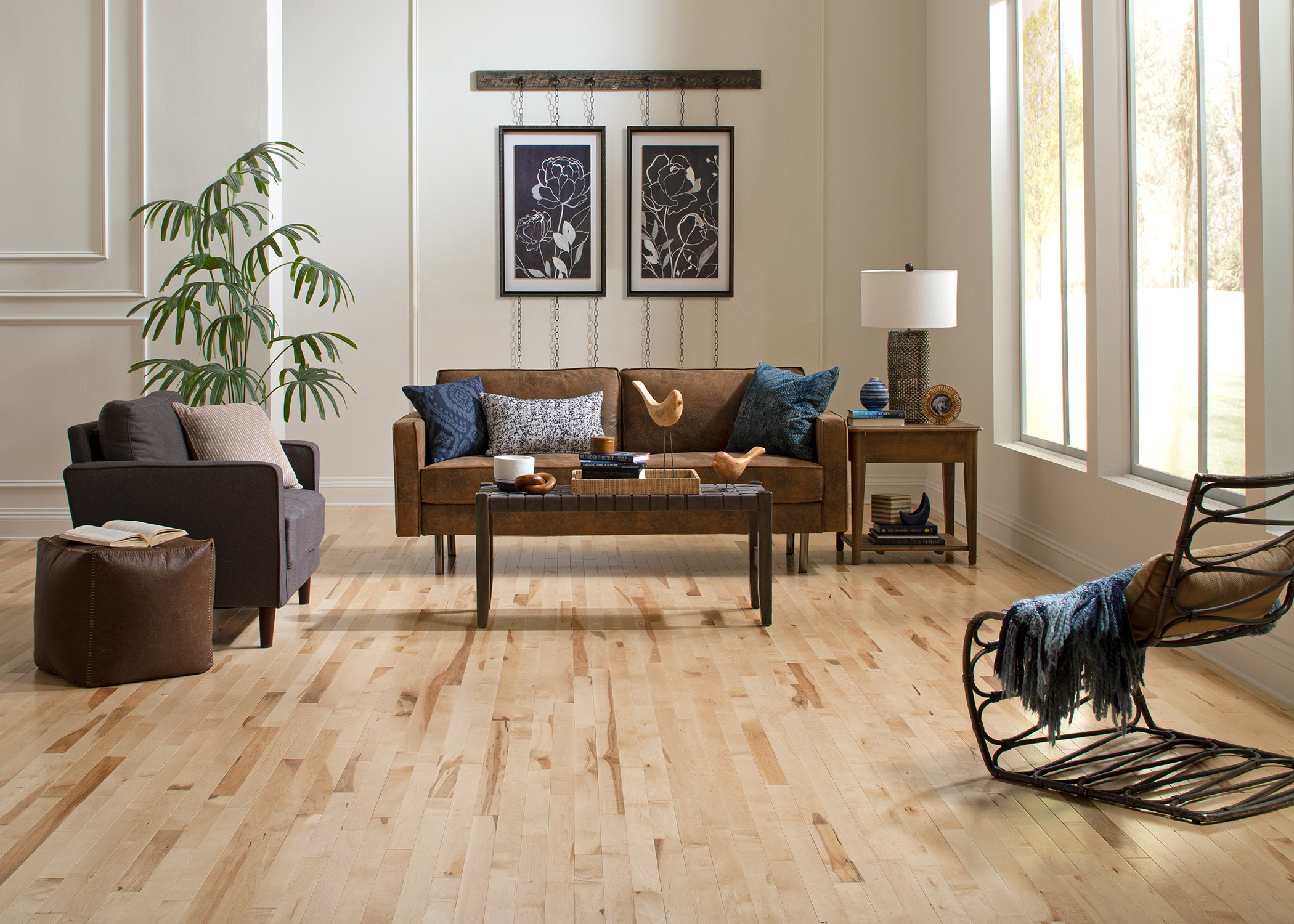 blonde solid hardwood flooring in living room with dark brown sofa and rattan armless chair