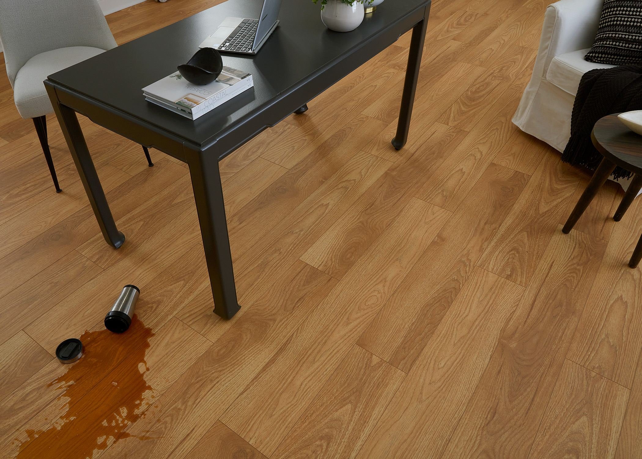 reddish brown waterproof hybrid resilient flooring in office with coffee spilled on floor next to black desk with laptop and upholstered desk chair