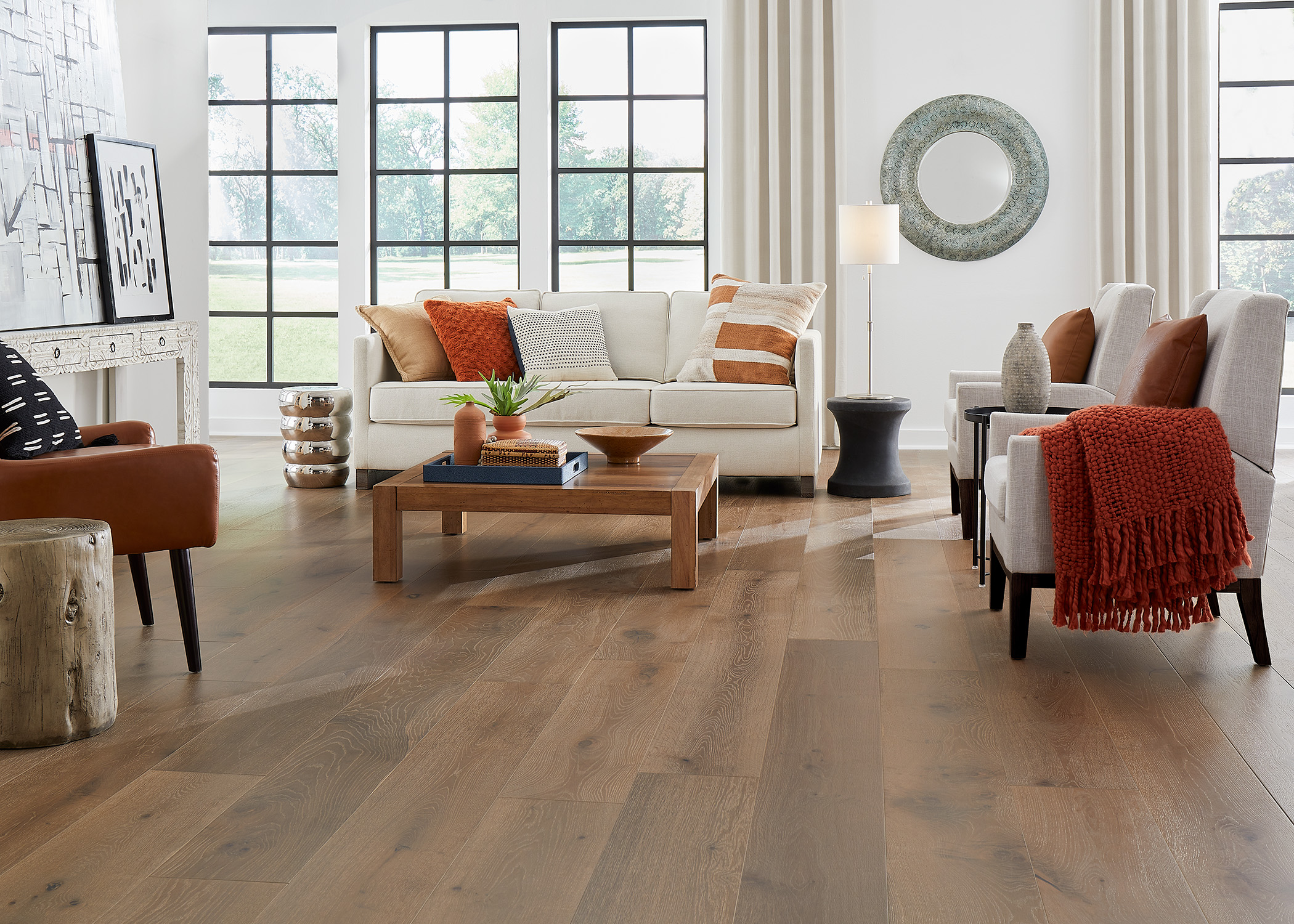 medium brown distressed engineered hardwood flooring in living room with cream sofa and chair with dark orange throw and pillows