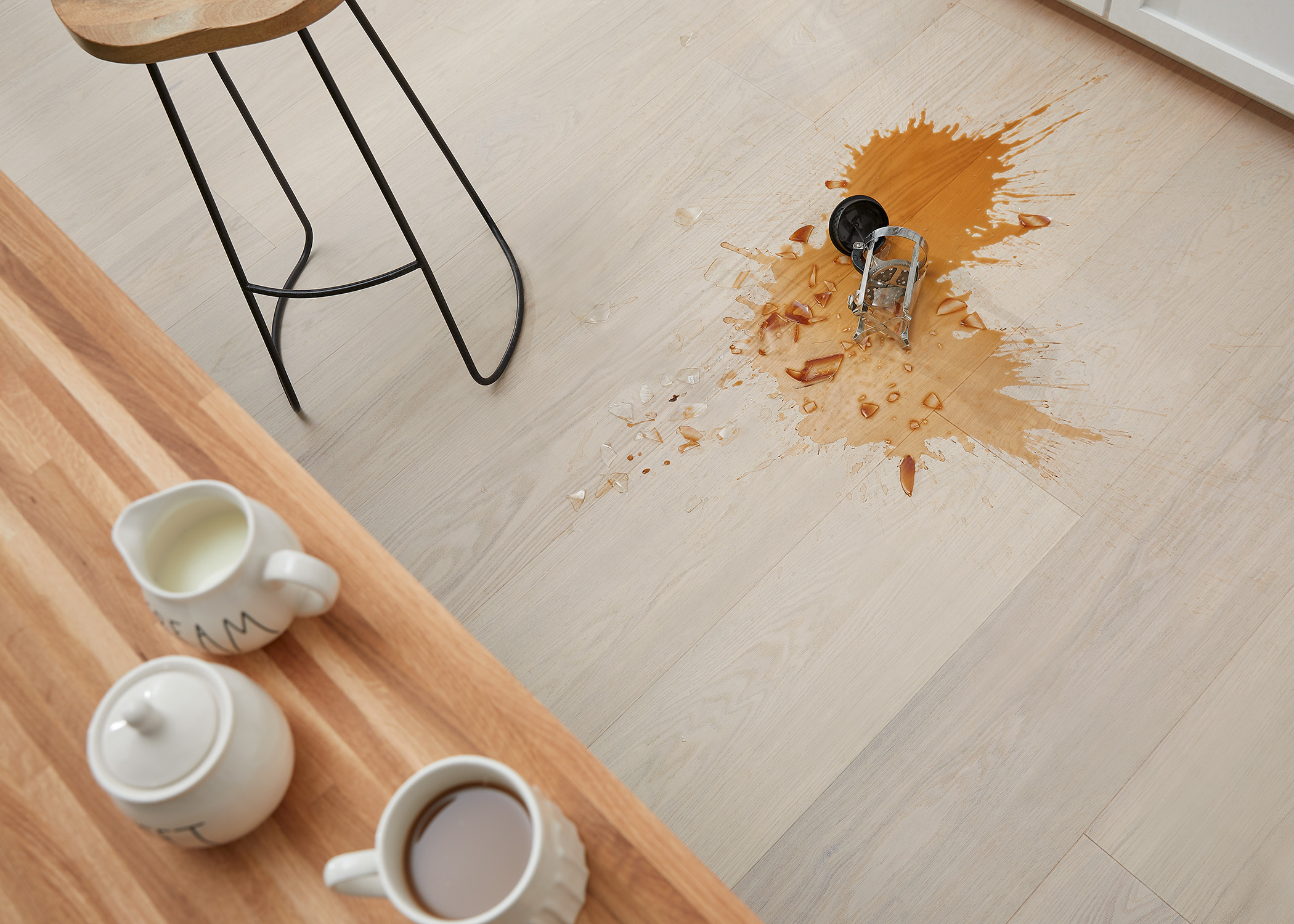 blonde water resistant engineered hardwood flooring in kitchen with spilled coffee on floor and broken French press