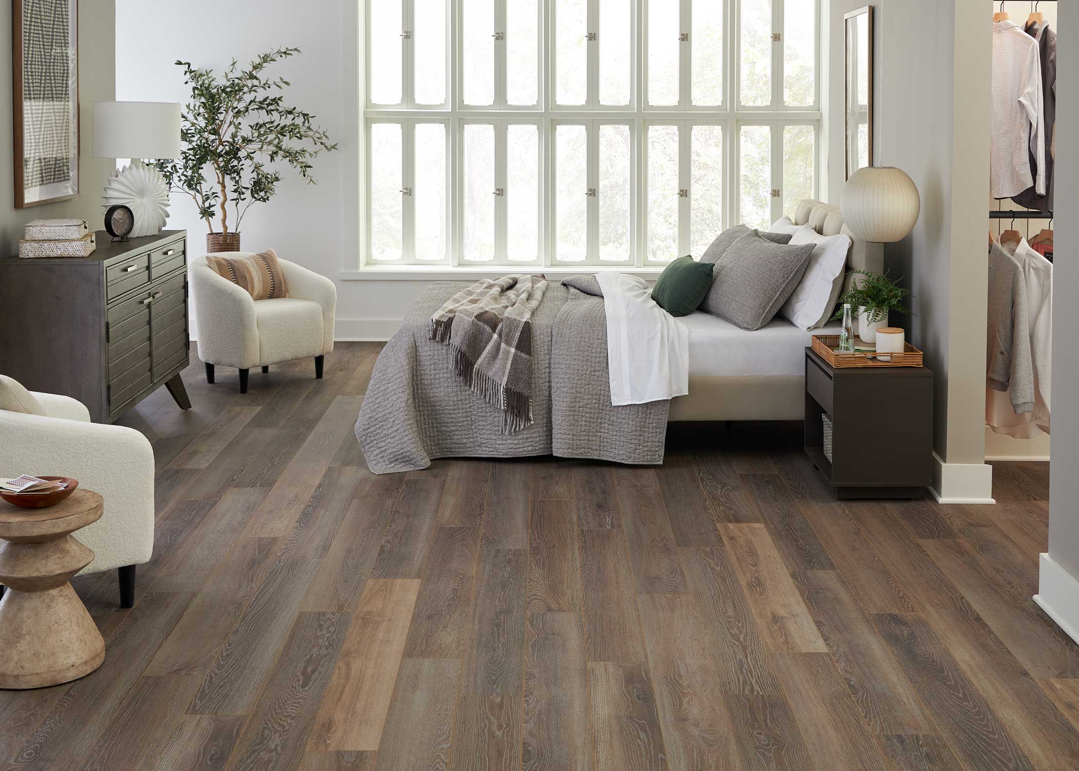 medium brown waterproof hybrid resilient flooring in bedroom with dark beige bedding plus dark brown tables and cream upholstered accent chairs