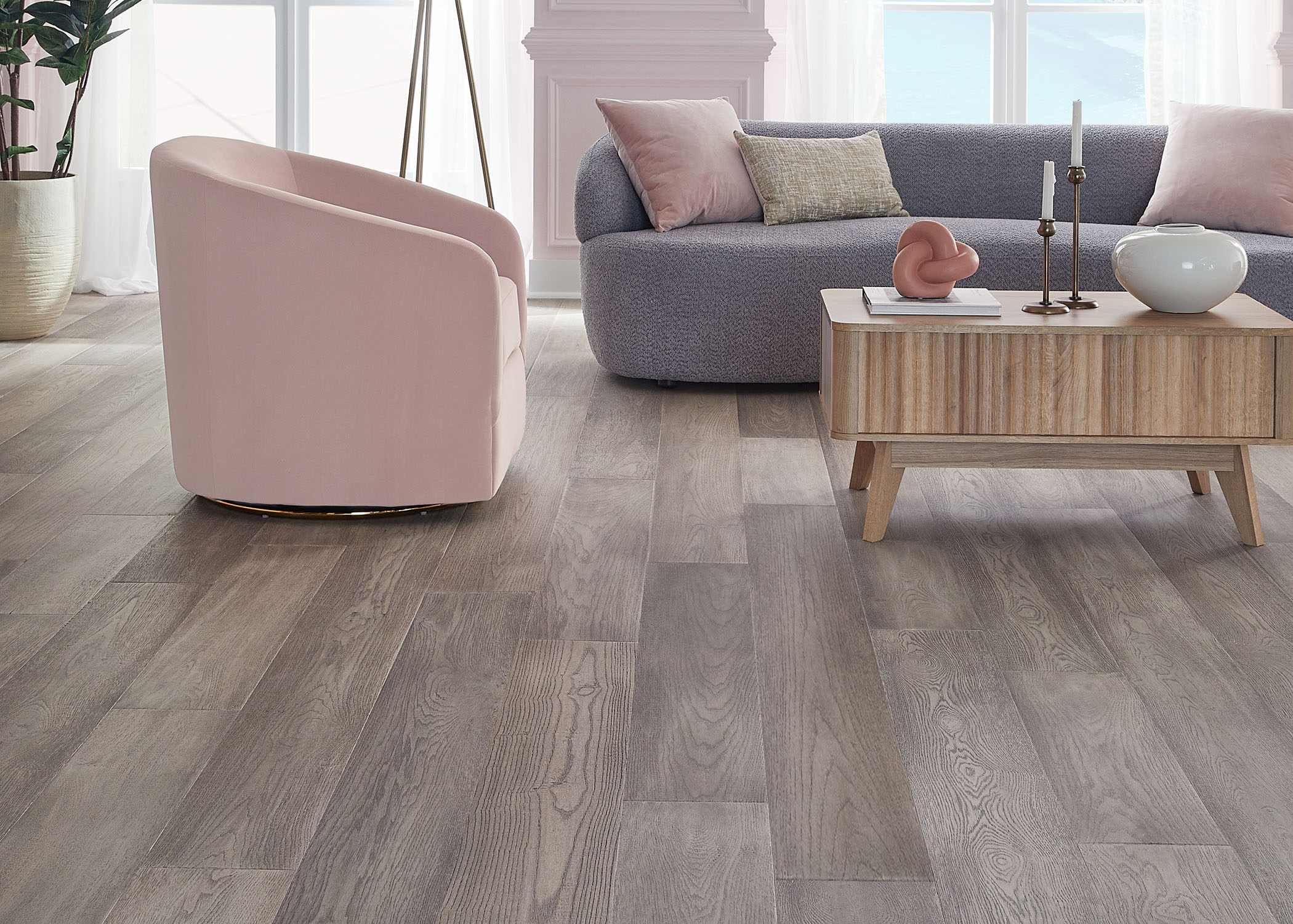 silver distressed engineered hardwood flooring in living room with gray sofa with pale pink accent pillows and pink barrel chair plus blonde wood cocktail table