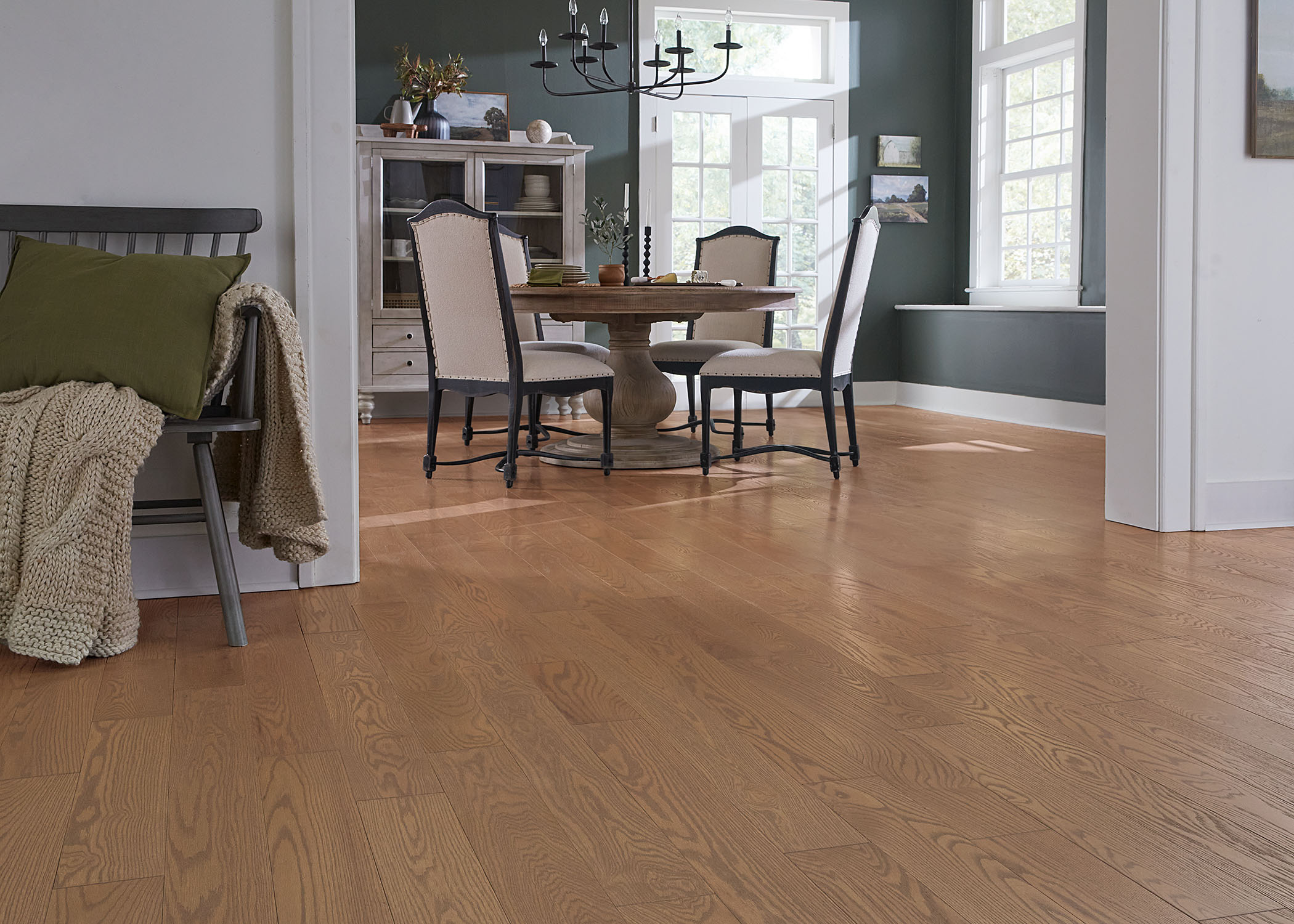 gold solid hardwood flooring in dining room with dark green walls and beige fabric dining chairs