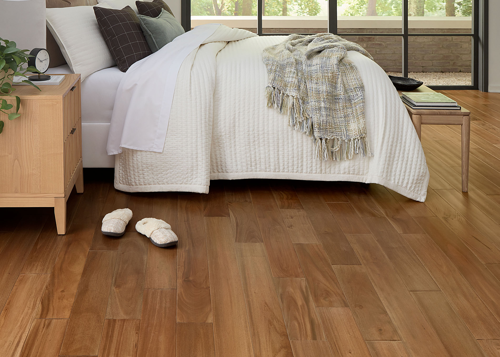 gold solid hardwood flooring close up in bedroom with off white bedding plus gray and taupe striped throw and off white slippers