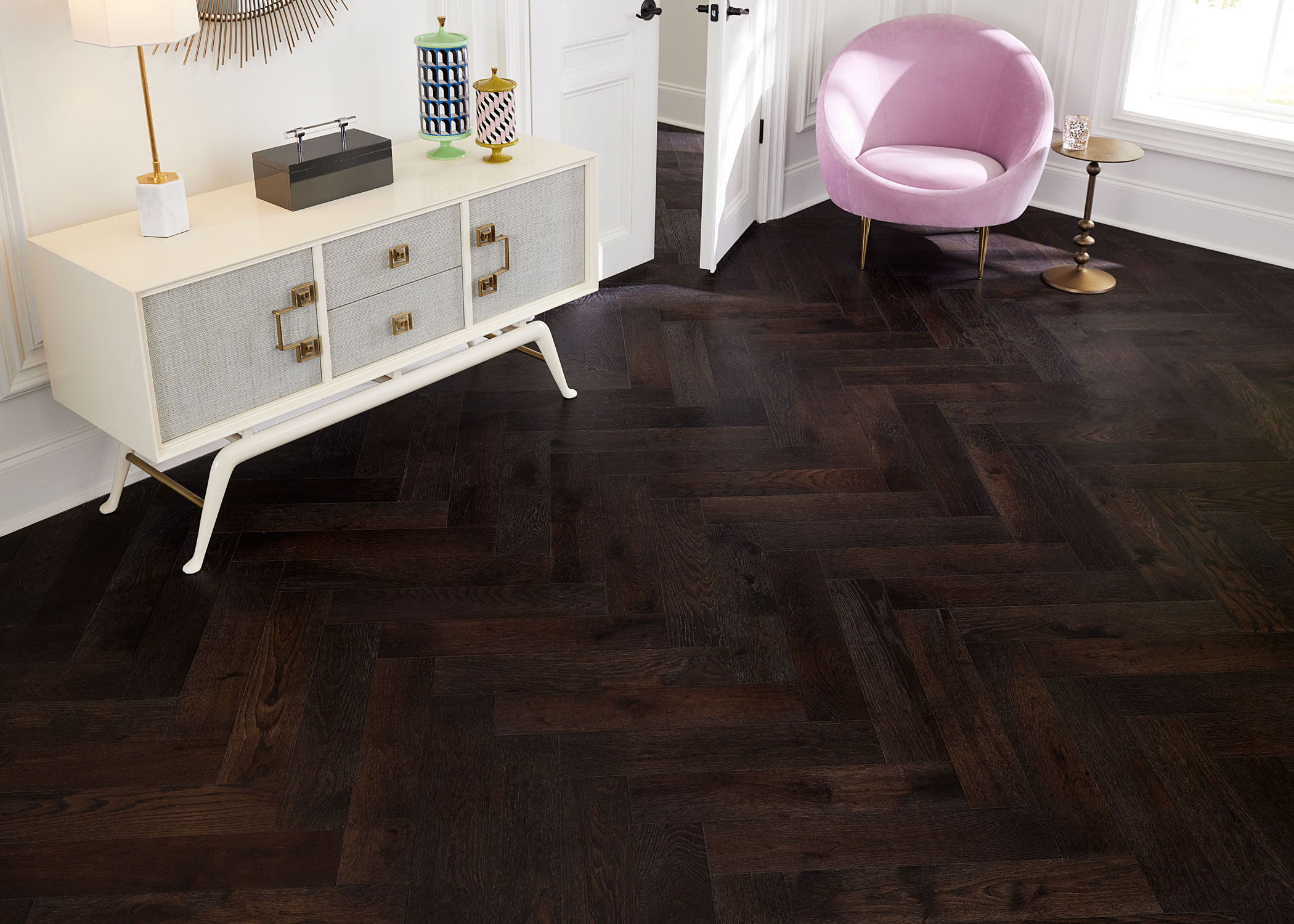 dark brown herringbone wire brushed engineered hardwood flooringin living room with pink velvet accent chair with gold legs plus off white console table with white and gold table lamp