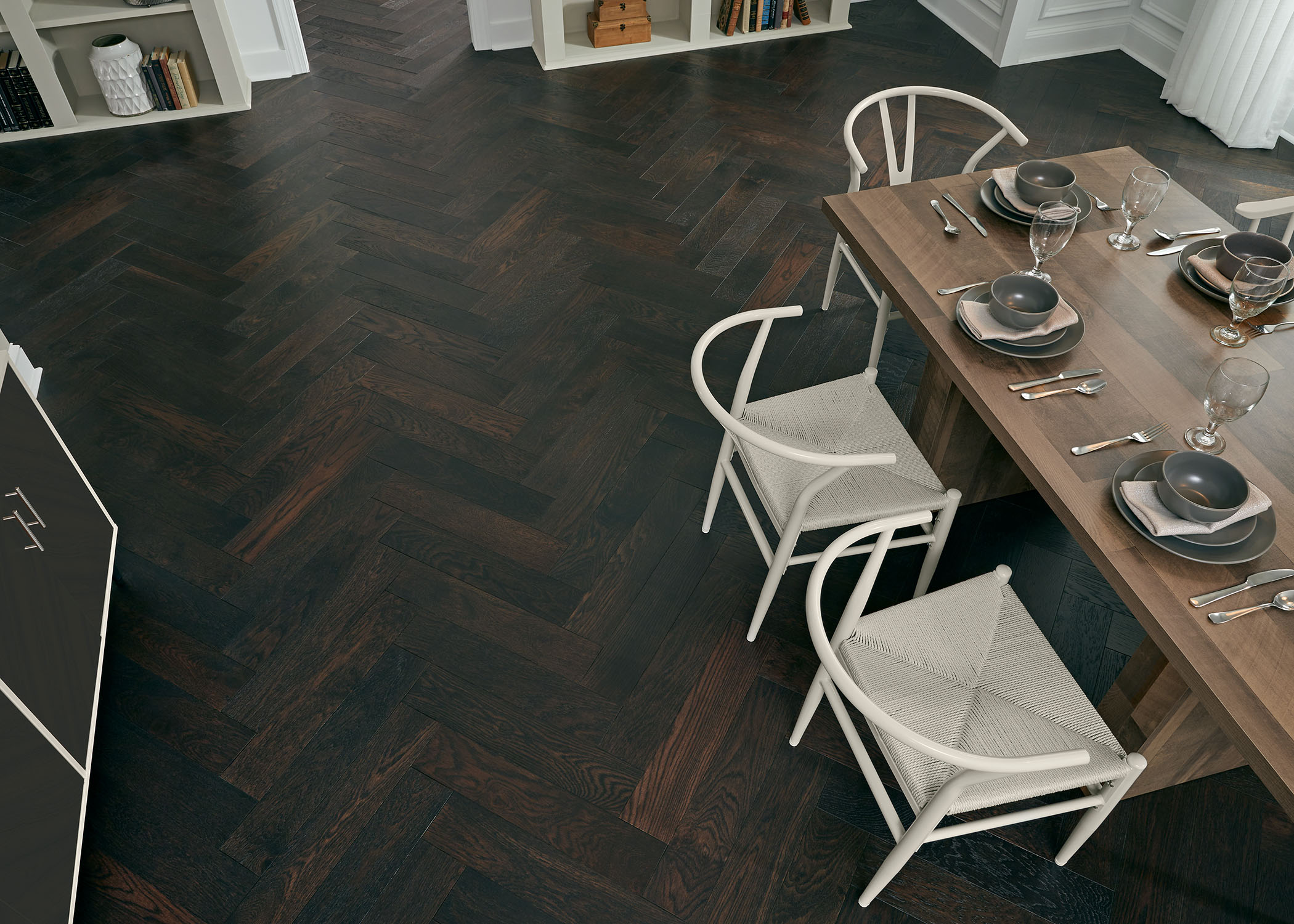 dark brown herringbone wire brushed engineered hardwood flooring overhead in dining room with wood dining table and cream chairs plus gray table setting