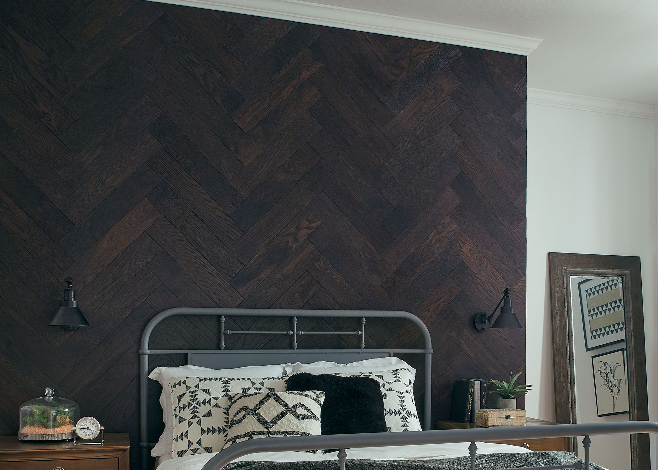 dark brown herringbone wire brushed engineered hardwood flooring as accent wall in bedroom with metal bed and gray quilt