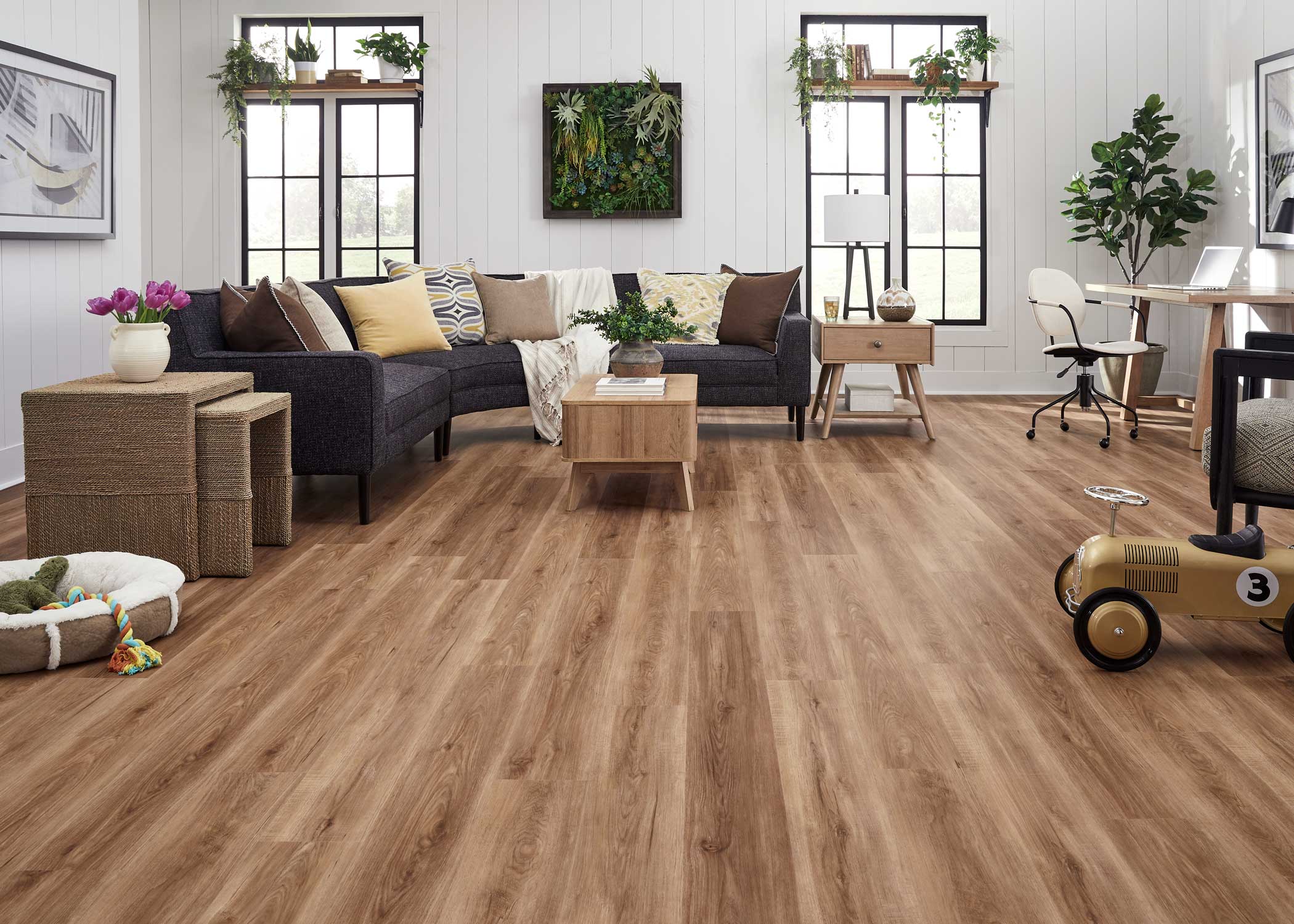 multi toned brown waterproof rigid vinyl plank flooring in living room with black upholstered sectional with blonde wood tables plus shiplap walls and butcher block window shelving with plants