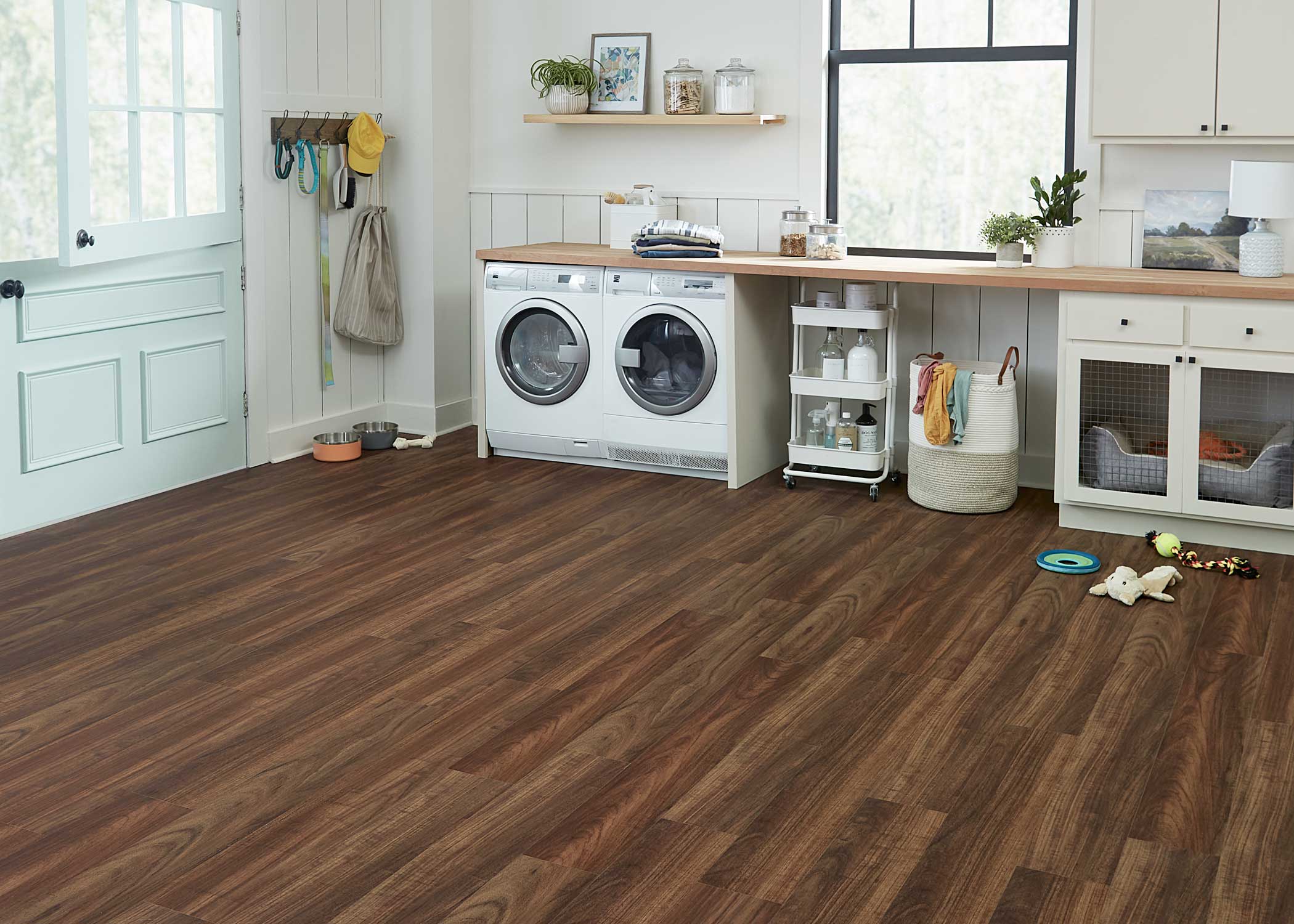 dark brown waterproof rigid vinyl plank flooring in laundry room with white washer and dryer plus butcher block counter and off white cabinets with built in dog crate