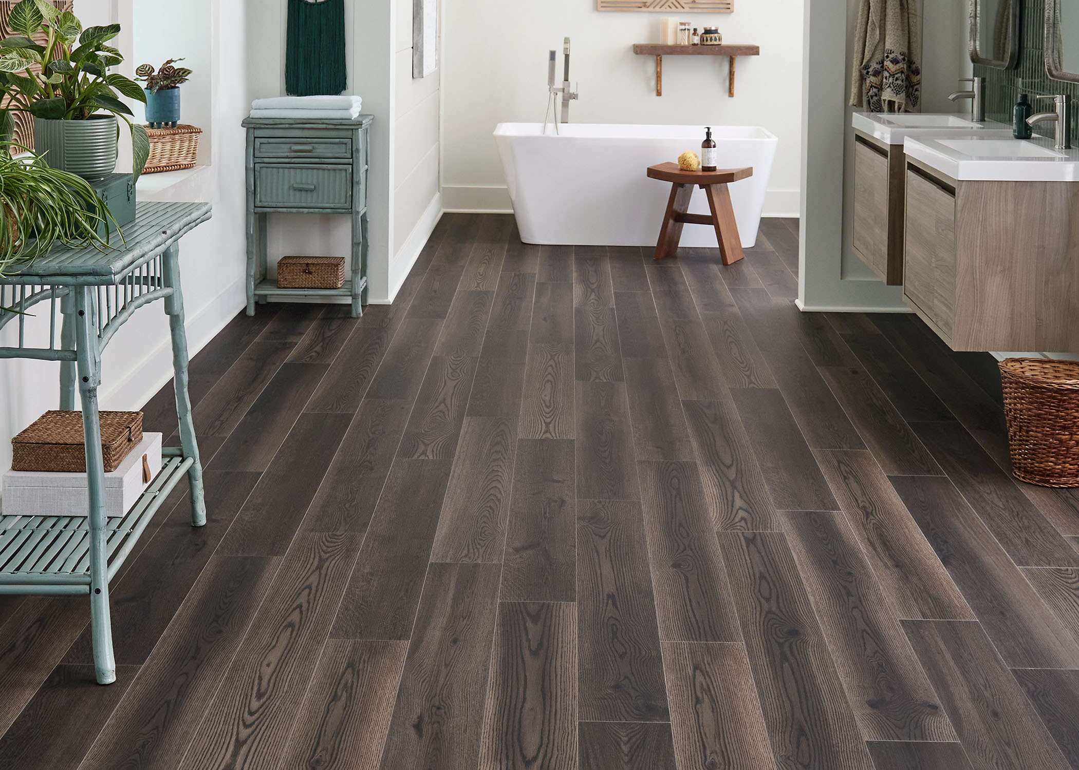 dark brown waterproof rigid vinyl plank flooring in bathroom with dual floating vanities plus rectangle bathtub with wood stool in front plus green rustic rattan tables