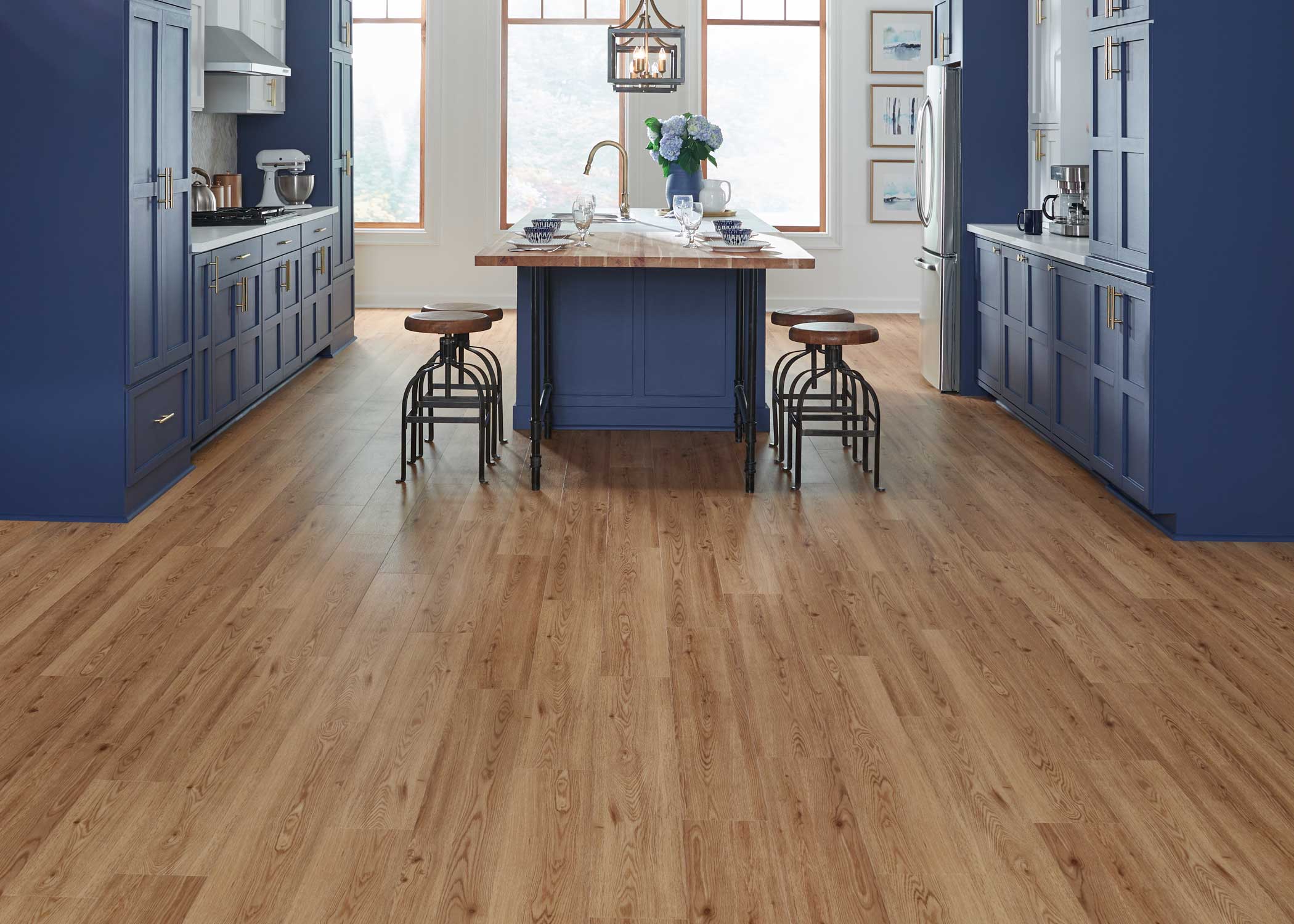 medium brown wood look waterproof rigid vinyl plank flooring in kitchen with blue floor to ceiling cabinets plus butcher block island and white countertops