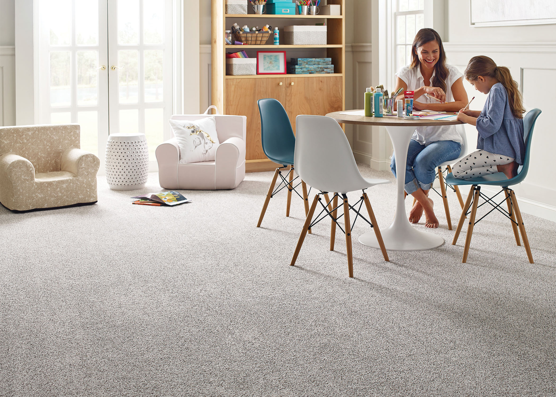 woman and young child in playroom with light colored carpet coloring at white table with white chairs