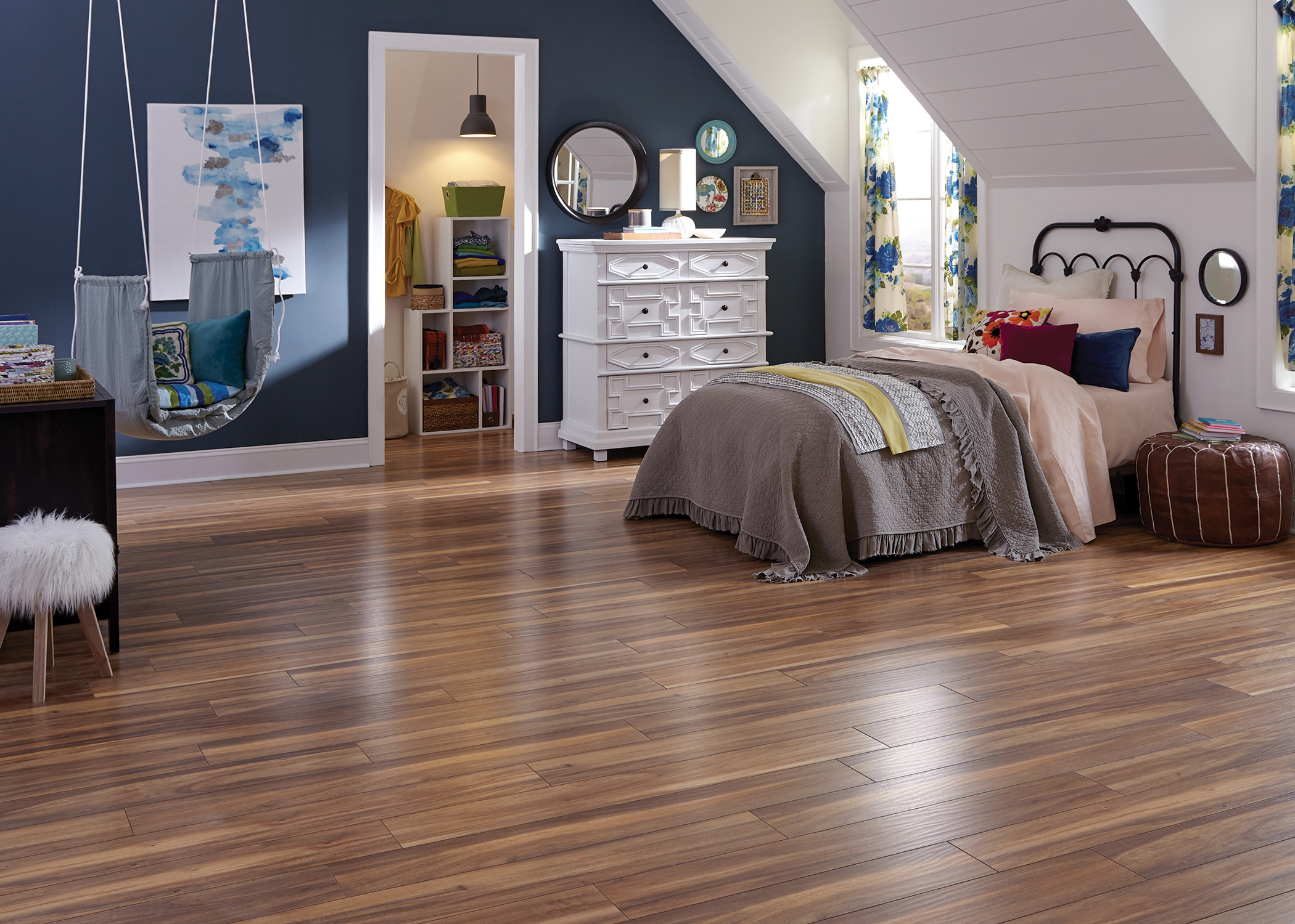 multi toned brown waterproof laminate flooring in bedroom with wrought iron headboard with peach and gray bedding plus white dresser and chair swing