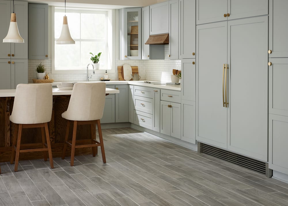 36 in. x 6 in. Oceanside Oak Gray HD Porcelain Tile in kitchen with blue gray cabinets plus white countertops and cream upholstered bar stools and white pendant lights