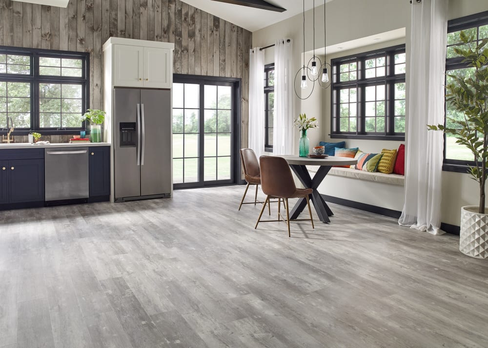 Moonlight Pine Rigid Vinyl Plank Flooring in open concept kitchen and dining with blue cabinets plus stainless steel appliances and round dining table with brown dining chairs and bench seating