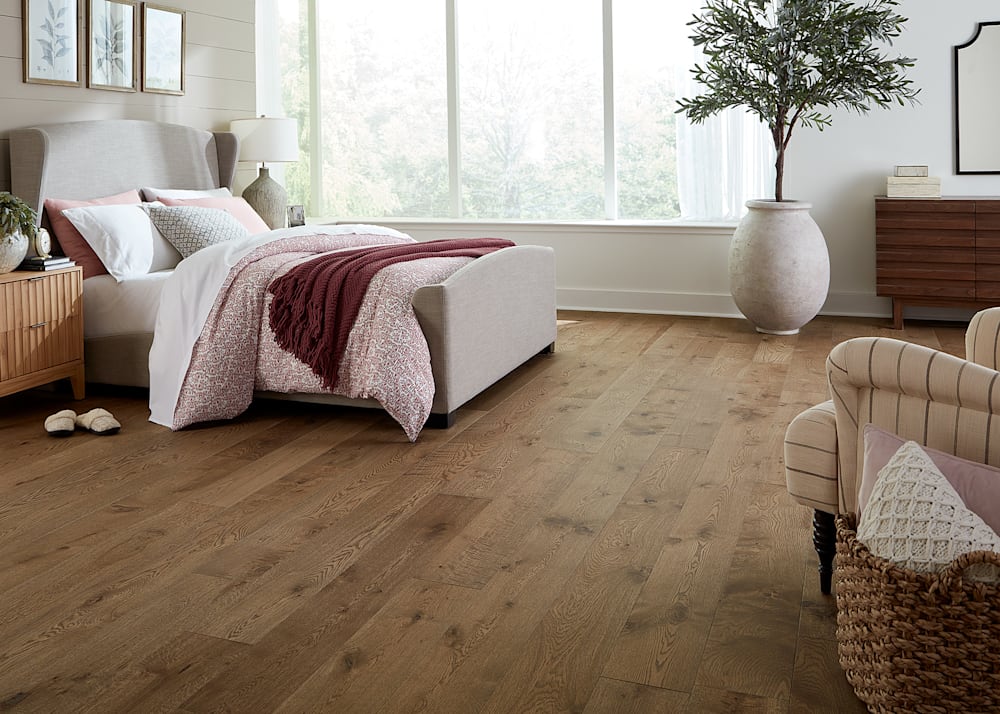 5/8 in. x 7.5 in. Monaco White Oak Engineered Hardwood Flooring in bedroom with beige upholstered bed plus large clay pot with decorative tree and striped upholstered chair