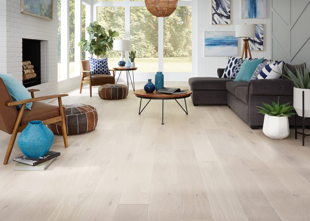 5/8 in. x 7.5 in. Barcelona White Oak Engineered Hardwood Flooring in living room with dark brown sectional with accent pillows in shades of blue plus brown leather and wood side chairs and white brick fireplace