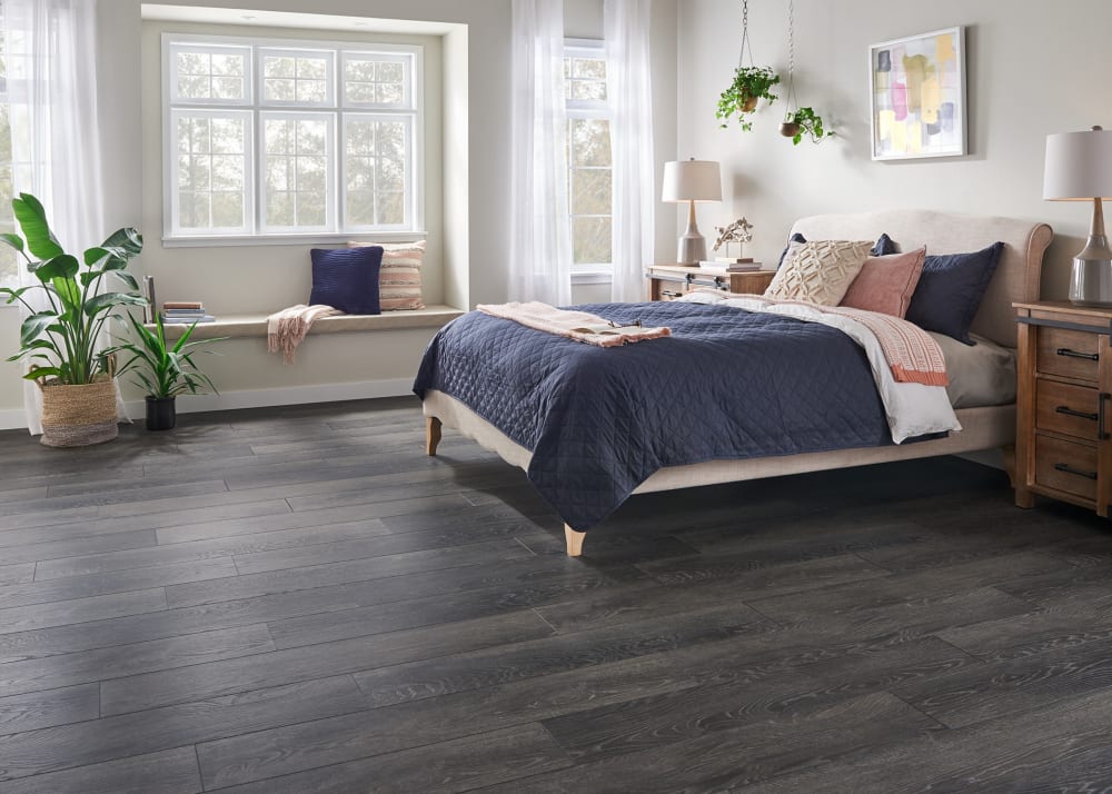 12mm Midnight Oak 72 Hour Water-Resistant Laminate Flooring in bedroom with beige headboard and blue bedding plus window seat with blue and pink accent pillows
