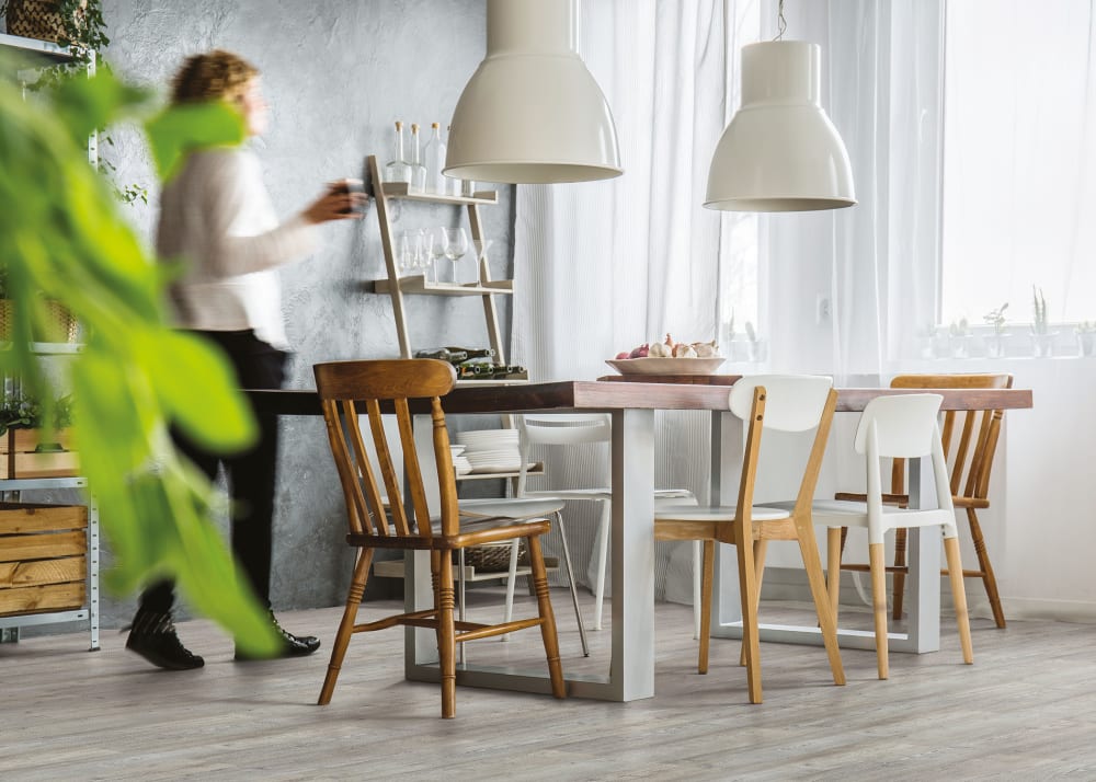 Arcadian Arctic Pine Cork Flooring greige cork floor in dining room with wood table and chairs plus white pendant lighting with person walking past table