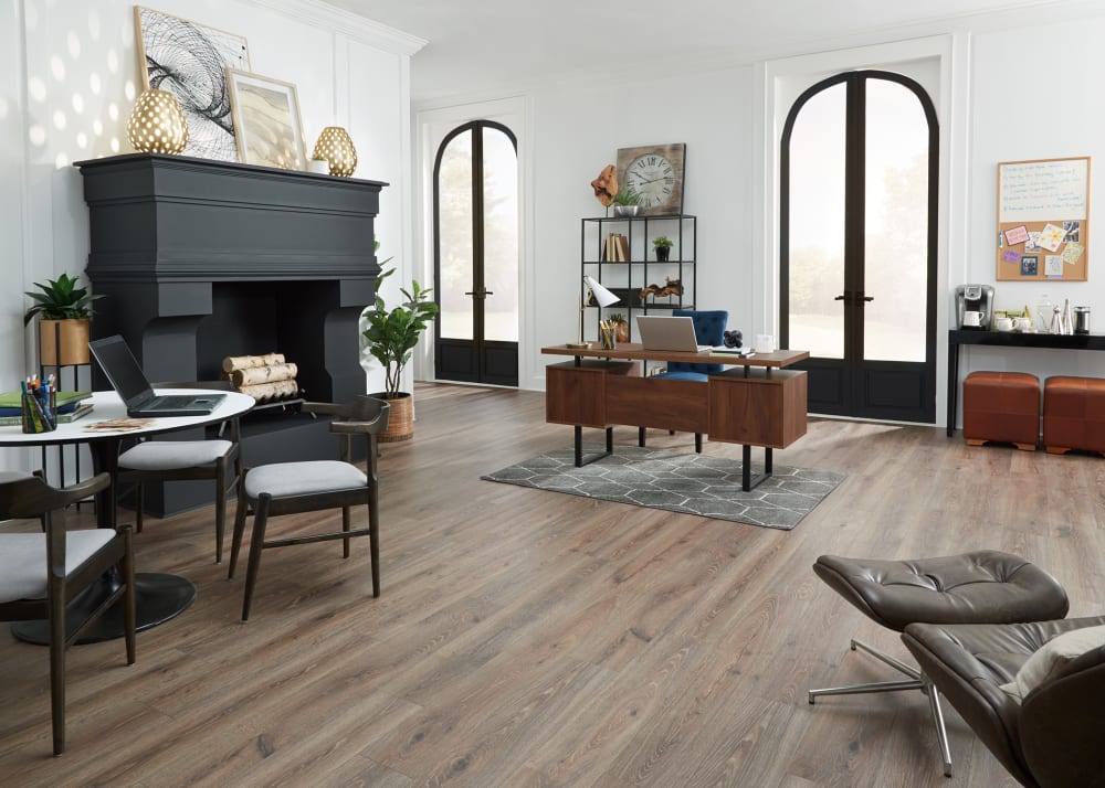 9mm with Pad Sagrada Oak Waterproof Hybrid Resilient Flooring in office with oversized black fireplace plus dark brown wood desk and small round table with three dark brown and gray chairs