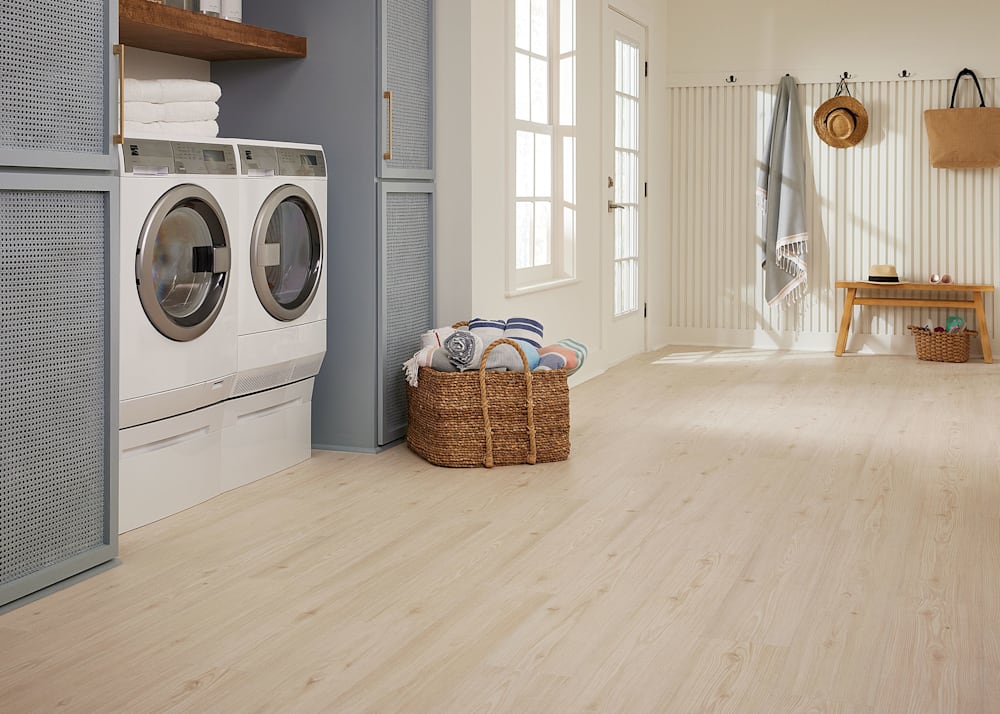 9mm with Pad Voyager Pine Waterproof Hybrid Resilient Flooring in laundry room with white washer and dryer plus light brown basket with towels and gray cabinets