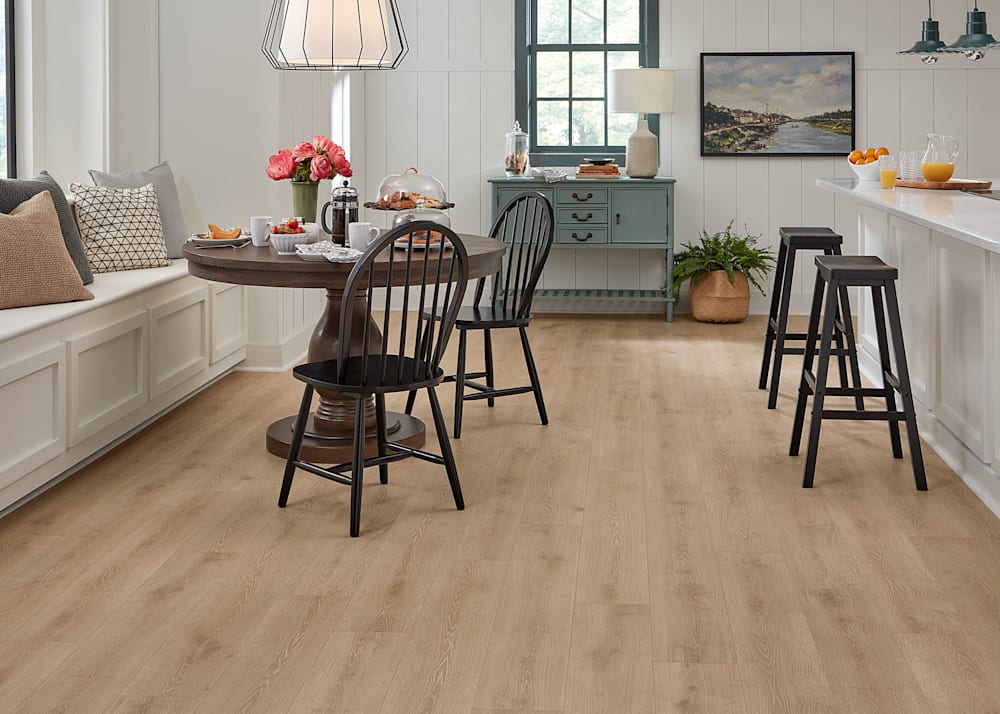 9mm with Pad Lake Lager Oak Waterproof Hybrid Resilient Flooring in kitchen with down brown round dining table with black dining chairs and bench seating with accent pillows and black bar stools