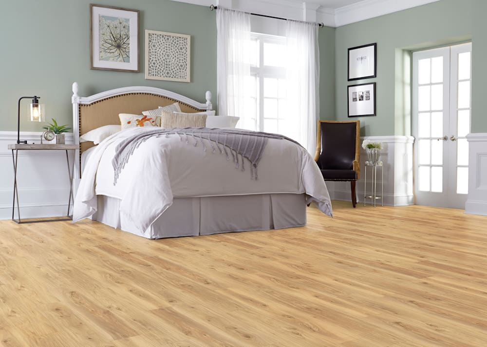 5mm with Pad Marigold Elm Rigid Vinyl Plank Flooring in bedroom with white headboard and white bedding plus black leather chair and french doors