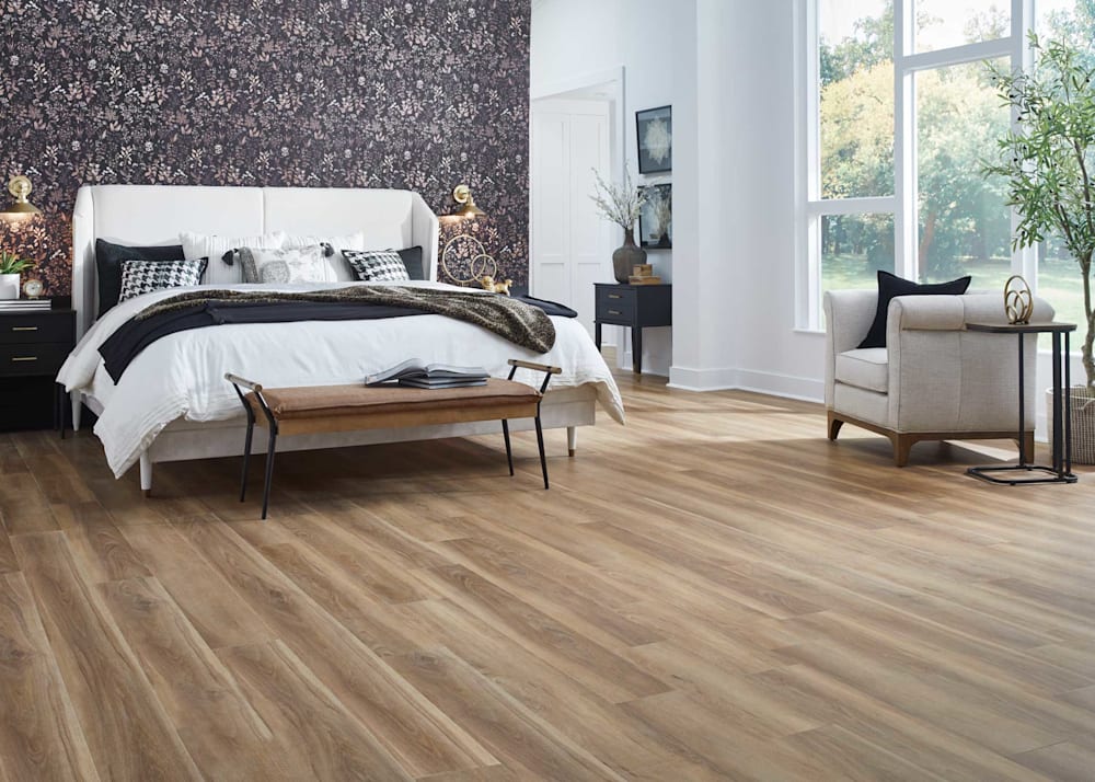 5mm with Pad Shoreway Oak Rigid Vinyl Plank Flooring in bedroom with white upholstered bed with white bedding plus black and white floral wallpaper and beige upholstered accent chair and brown leather bench