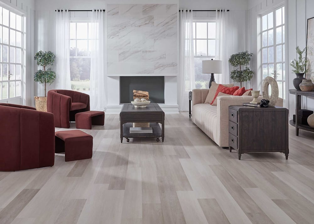 5mm with Pad Dexter Oak Waterproof Rigid Vinyl Plank Flooring in living room with cream upholstered sofa plus eggplant upholstered accent chairs and dark brown tables plus white fireplace with porcelain tile front