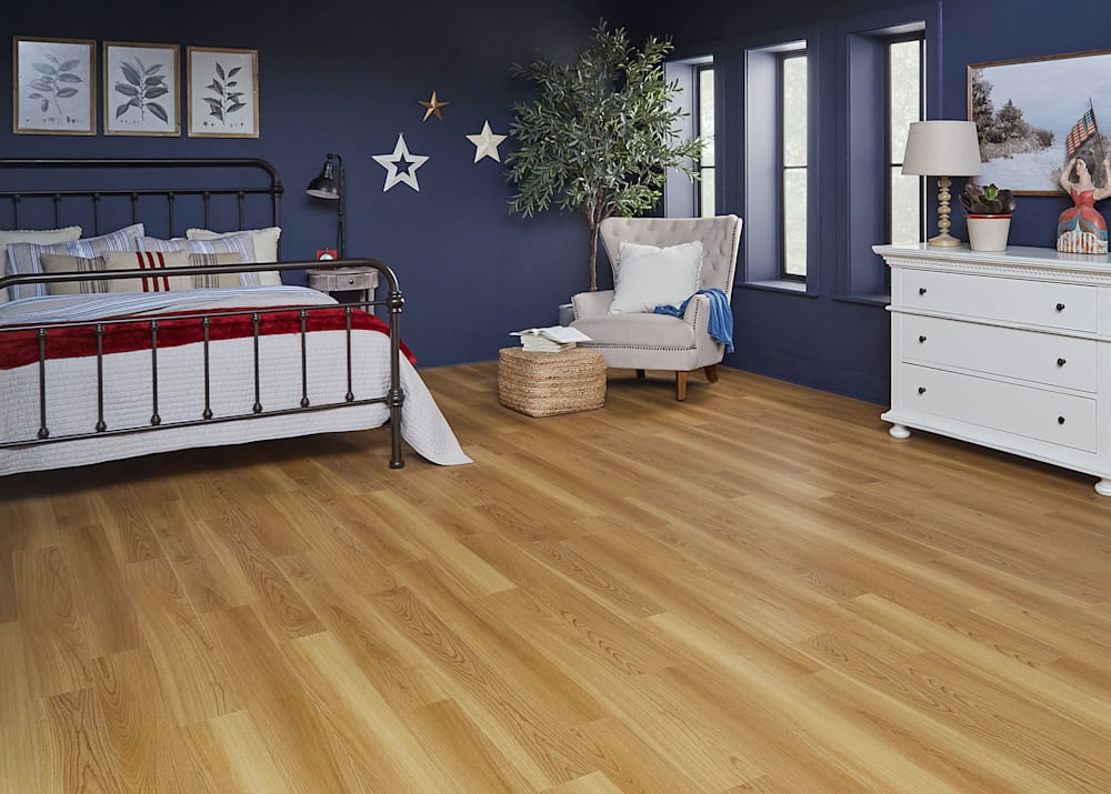 5mm with Pad Cumberland Cherry Waterproof Rigid Vinyl Plank Flooring in bedroom with black wrought iron bed with red white and blue bedding plus white stars on a dark blue accent wall and cream upholstered accent chair and white dresser