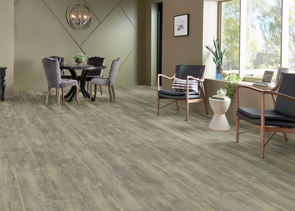8mm with Pad Duskwood Hickory Waterproof Rigid Vinyl Plank Flooring in open concept dining and living area with oval dining table with gray velvet chairs plus dark wood and gray upholstered accent chairs with small side table