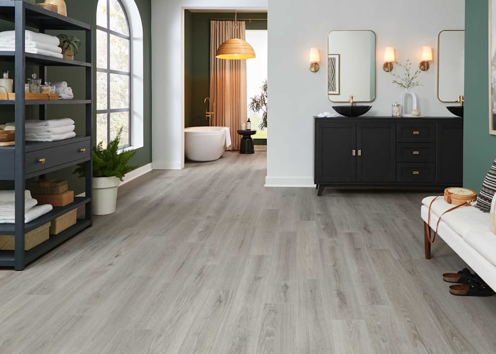 8mm with Pad Moonflower Bay Oak Waterproof Hybrid Resilient Flooring in bathroom with black vanity and white oval bathtub with gold fixtures and black cabinet