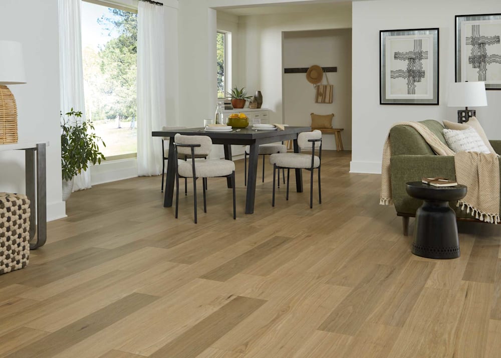 8mm with Pad Tupelo Honey Oak Waterproof Hybrid Resilient Flooring in open concept dining and living room with dark brown dining table with beige upholstered dining chairs and dark green upholstered sofa with beige throw and dark brown end table