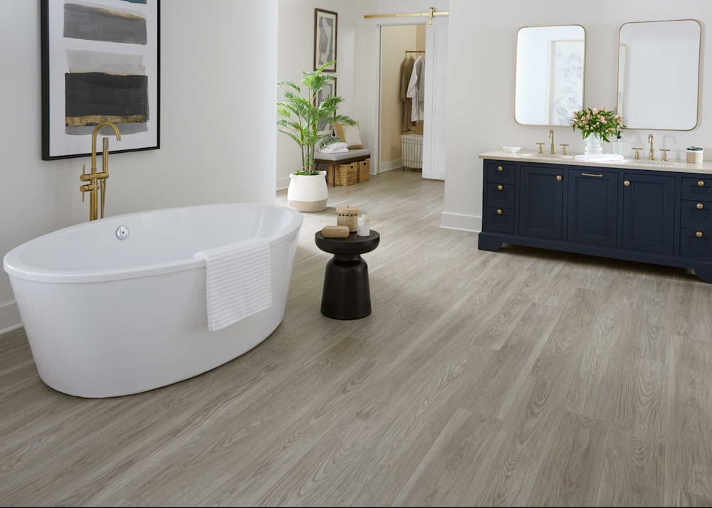 7mm with Pad Cordova Coast Oak Waterproof Rigid Vinyl Plank Flooring in bathroom with oval freestanding tub plus dark blue dual vanity and view into walk in closet with barn door