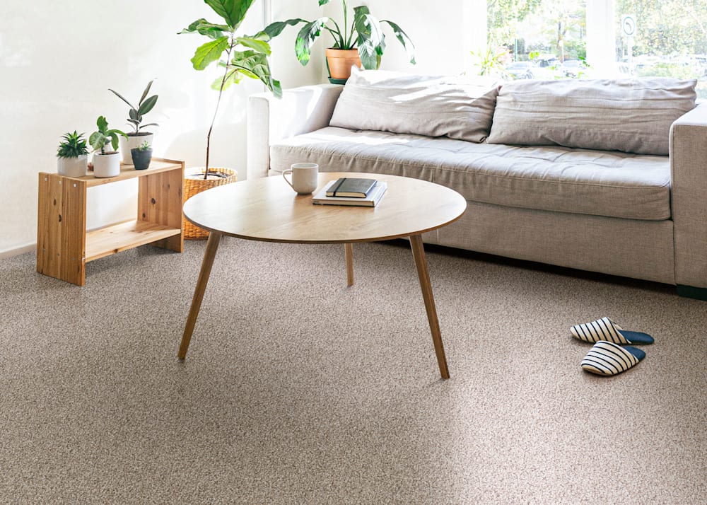 Graysdale Path Carpet in Buff in living room with beige sofa and light wood accent tables plus blue and white stripped slippers on floor